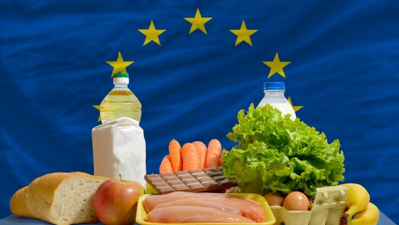 EU flag behind assorted groceries including vegetables and meat